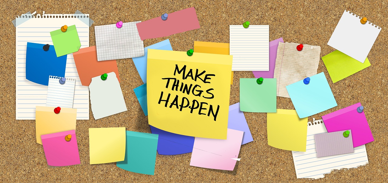 Several post-it notes pinned on a cork board, one of which says "Make things Happen" in black handwriting