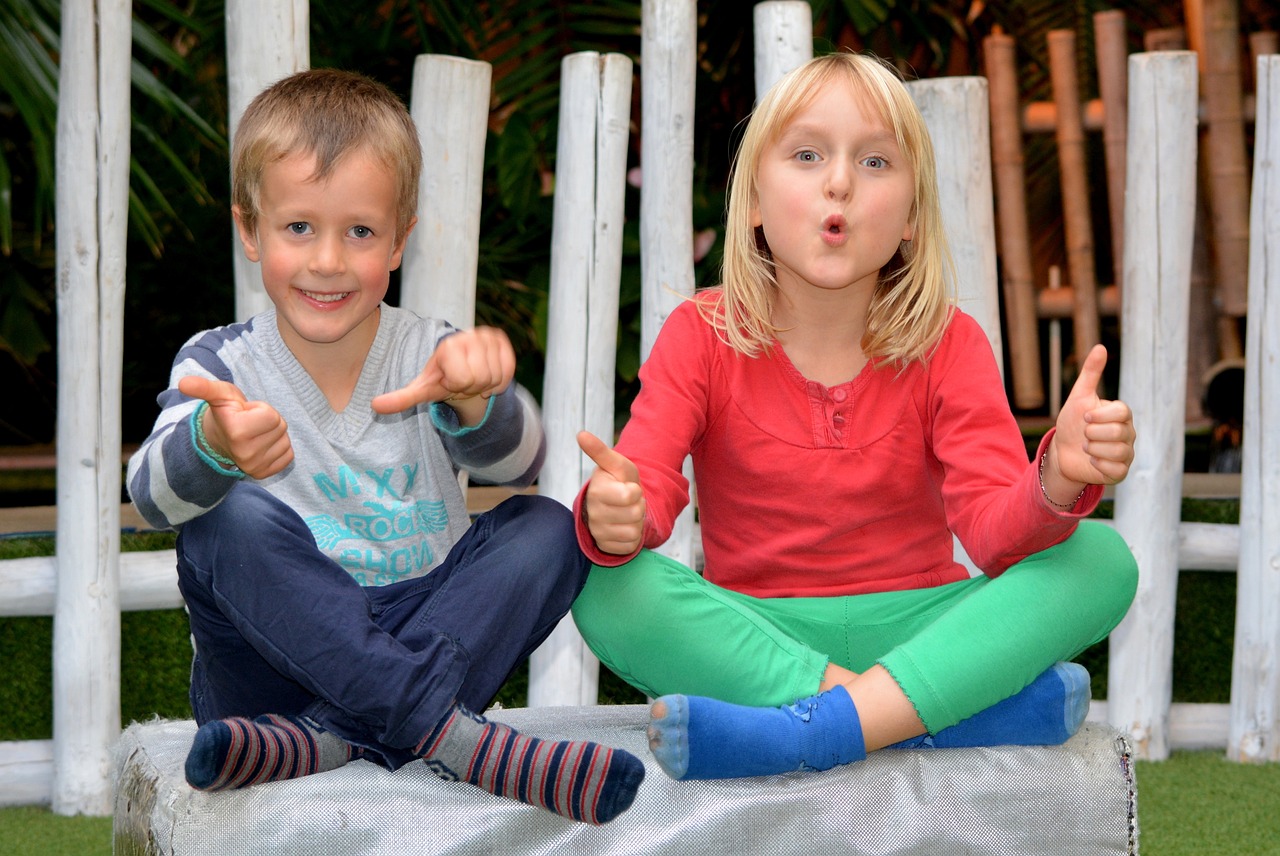 A boy and a girl sitting cross-legged, smiling and giving thumbs up to the camera
