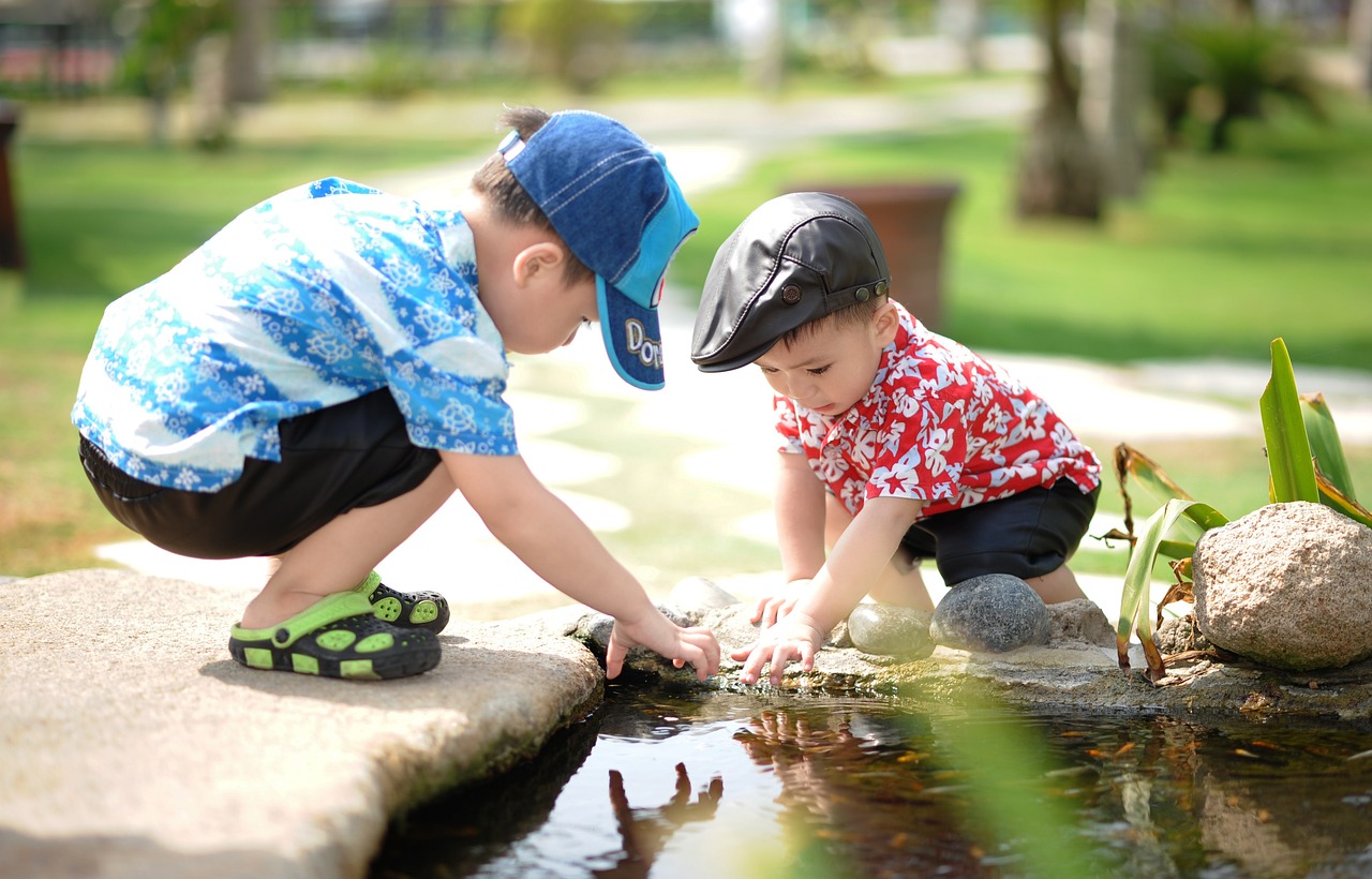 Two young boys bending down and playing in the edge of a pond