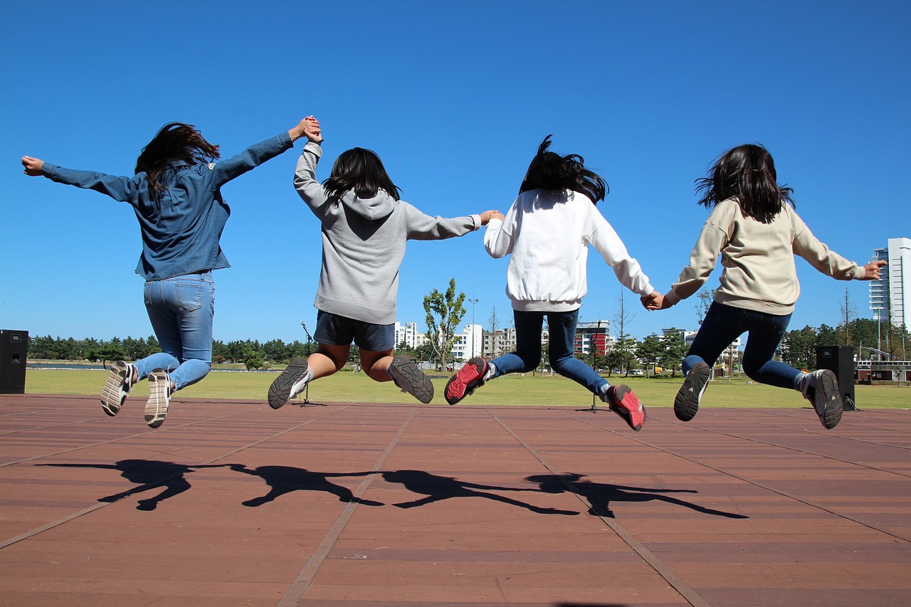 Four teenage girls, holding hands and jumping high into the air