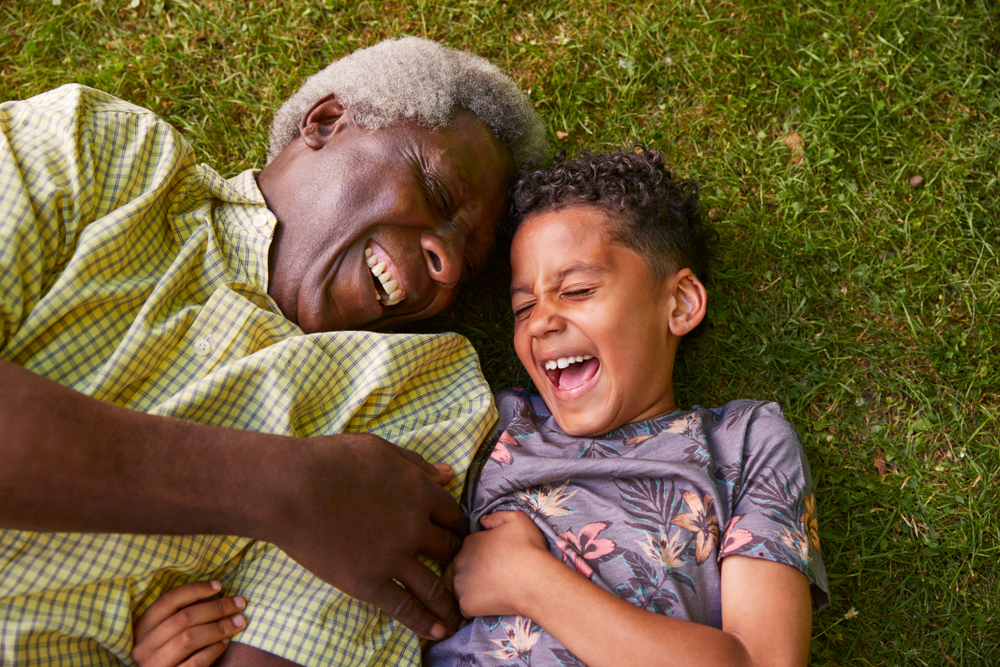 A young boy and older man lying on the grass, laughing