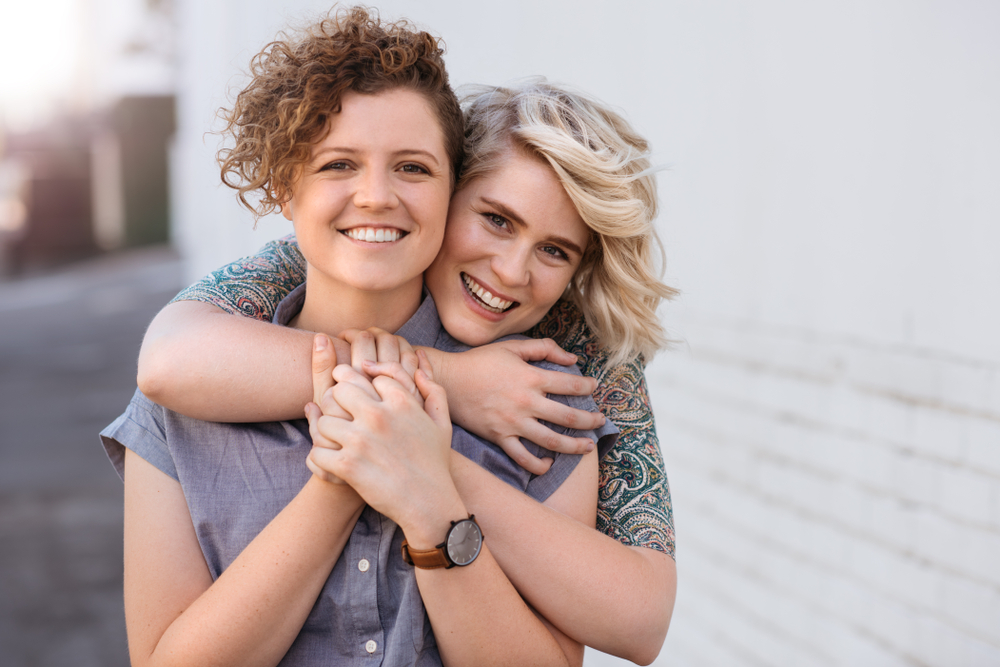 A smiling, young, same-sex couple hugging each other
