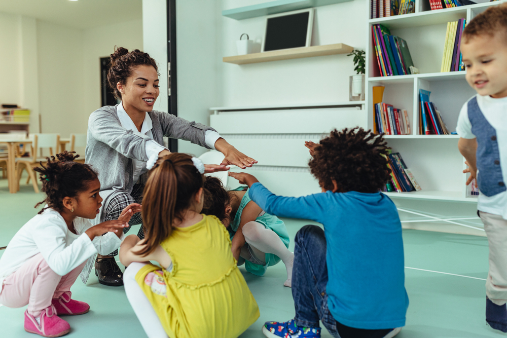 A teacher sitting on the floor, playing a game with young students in an informal classroom setting