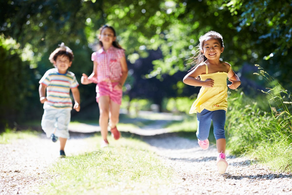Three children happily running towards the camera on a sunny countryside lane