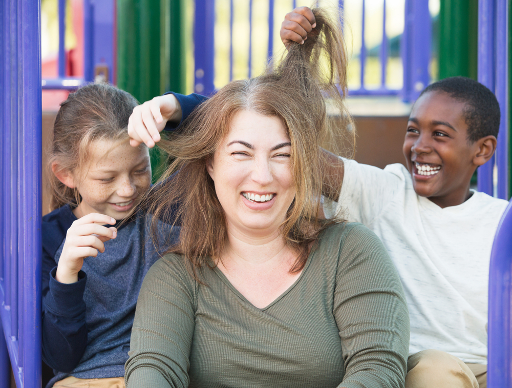 Laughing woman sitting with two smiling young boys playing with her hair