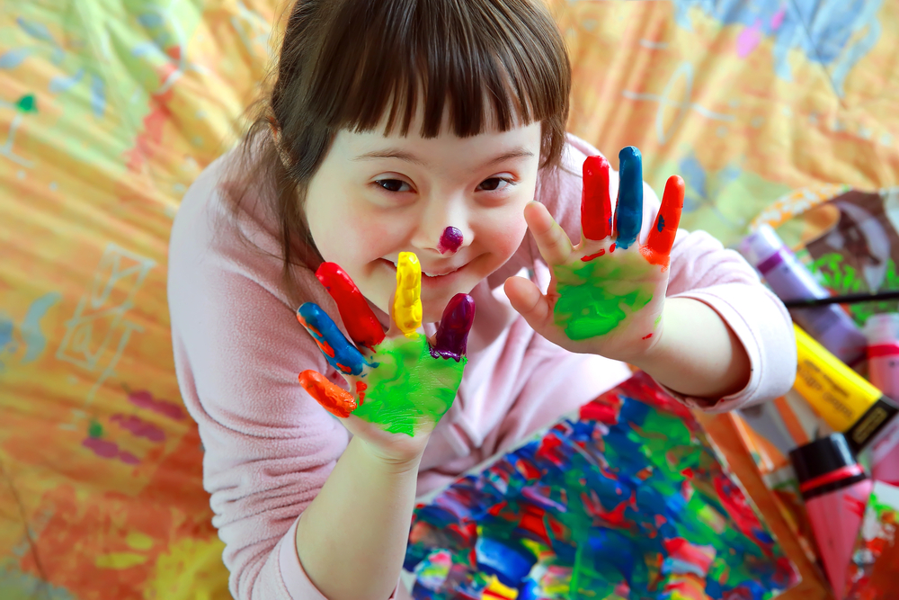 Cute little girl, with Down's Syndrome, with painted hands, smiling up at the camera