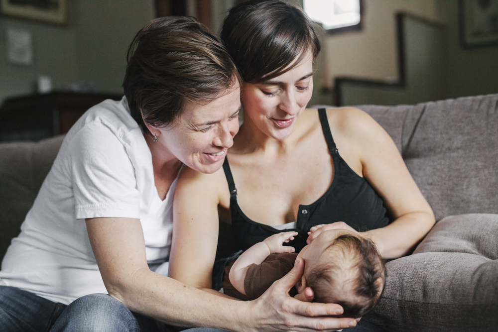A same-sex couple, smiling lovingly at their new baby