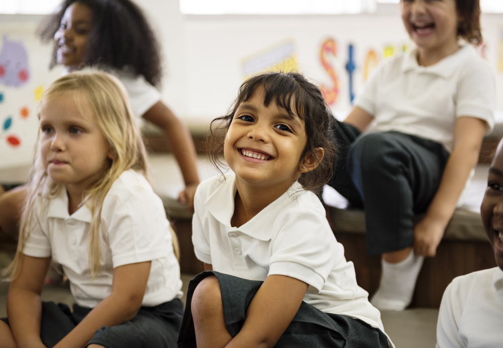 Smiling, young children sitting on the floor in school uniform