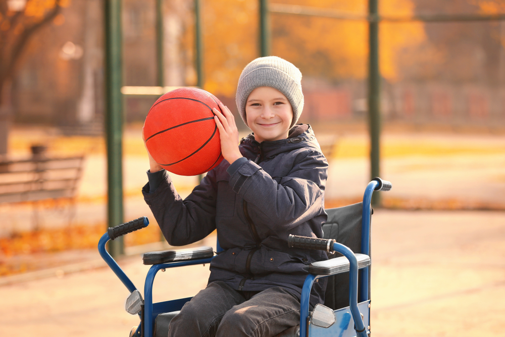 A smiling boy, in a wheelchair, holding a basketball, ready to throw it