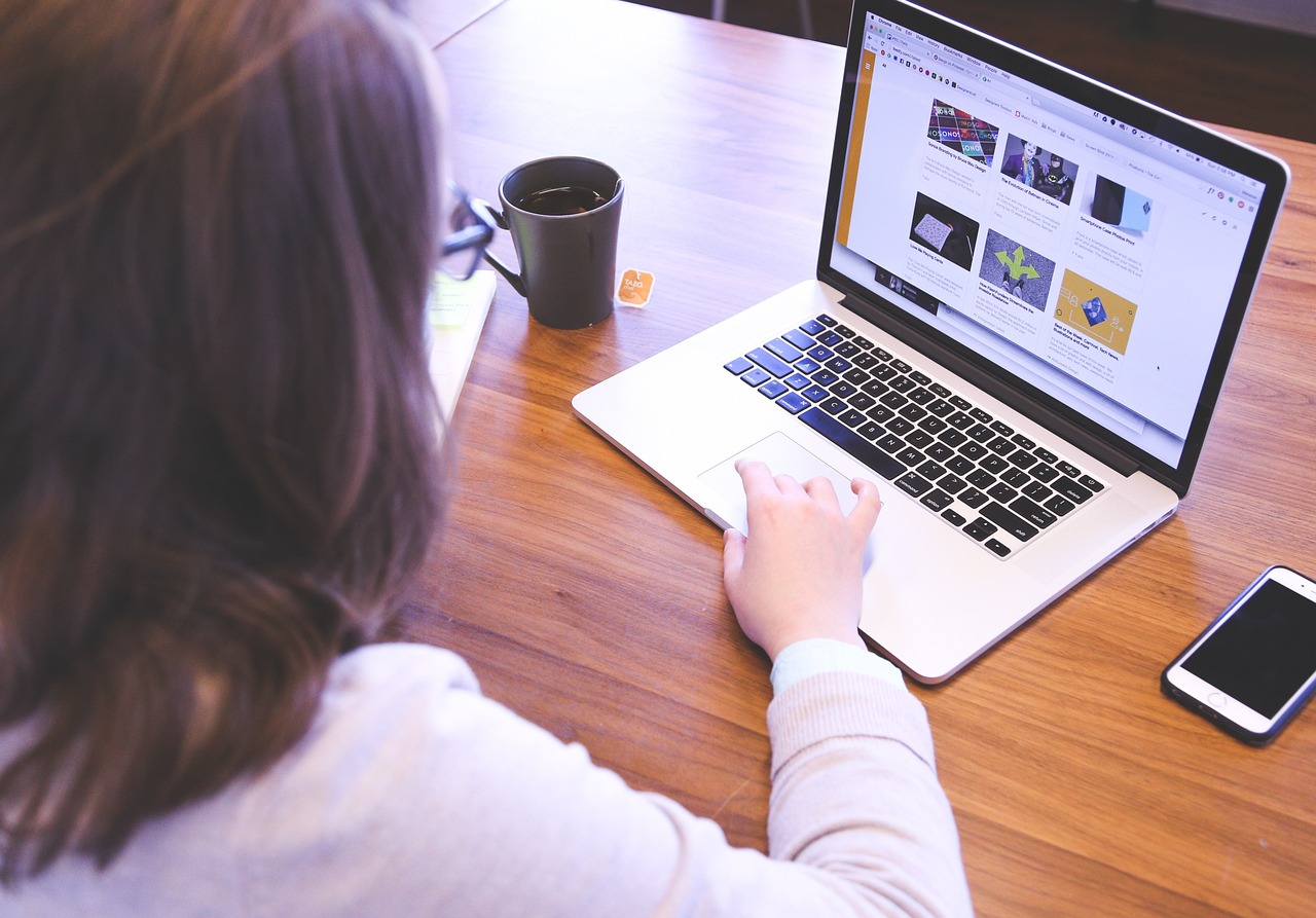 A woman using a laptop, with her phone and a cup of tea next to her on the desk