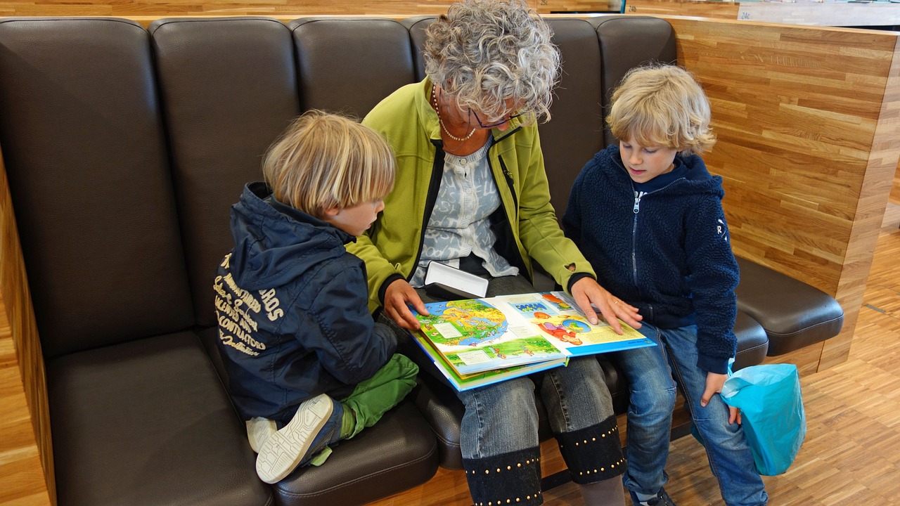 An older lady, sitting on a sofa, reading a book to two attentive, young boys